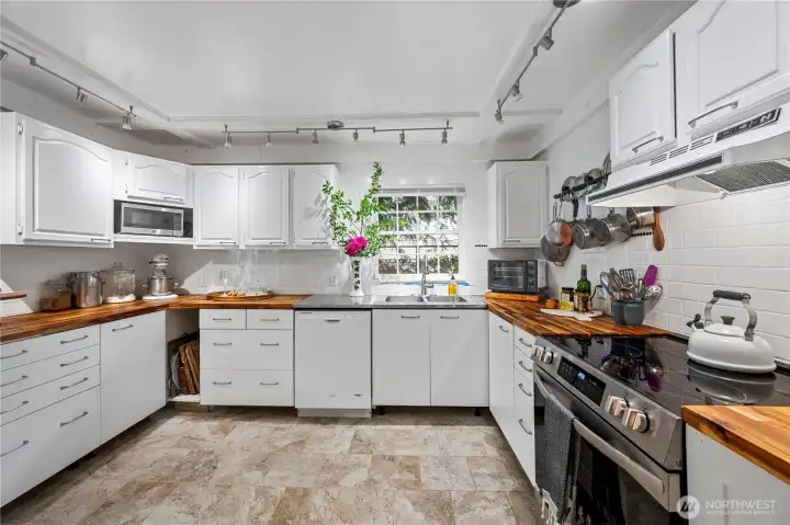 Kitchen features several work stations, butcher block countertops and tiled floor right off laudnry room