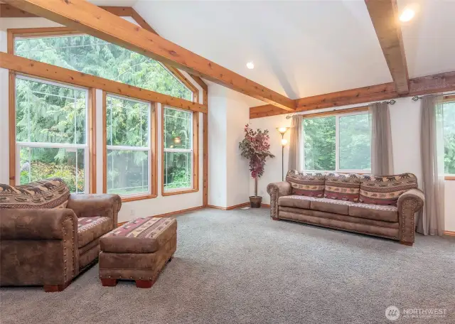 Spacious, furnished living room highlighted by detailed millwork, exposed beams, and wood-wrapped windows.