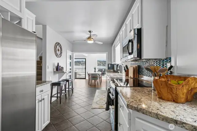 The lovely galley kitchen features stainless appliances, shaker cabinets, marble counters, and tile floors.