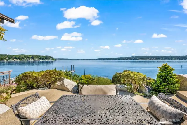 Step from the great room to a stunning waterside patio framed by lush landscaping, a carved granite bench, and serene southern views.