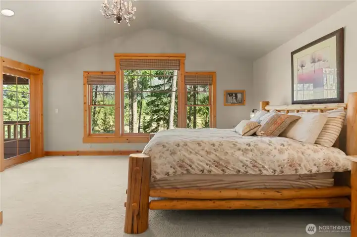 Spacious master bedroom with vaulted ceiling, abundant natural light, and stunning forested views. Private balcony access enhances the serene retreat feel.