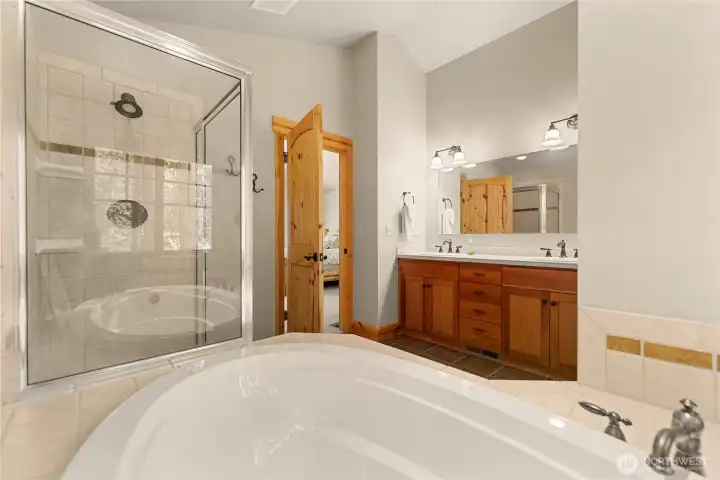 Luxurious primary bathroom featuring a soaking tub, walk-in tile shower, and dual vanity with warm wood cabinetry.