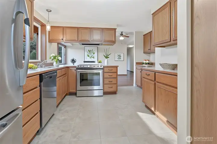 Kitchen features oak cabinets, stainless appliances including a newer kitchen aide downdraft range, an eating bar and opens to family room.  Virtually staged photo.