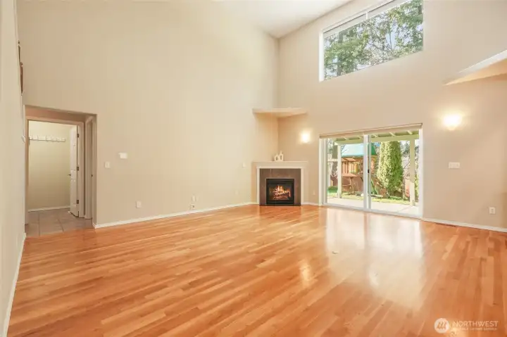 Soaring cathedral ceilings and dramatic walls of windows create an airy, light-filled great room designed to impress. Two upper windows are equipped with remote operation, enhancing both convenience and airflow. Gleaming hardwood floors add warmth underfoot, while a cozy gas fireplace anchors the space with inviting comfort. Seamlessly connected to the kitchen and covered patio, this open-concept living area is ideal for everyday living and effortless entertaining.