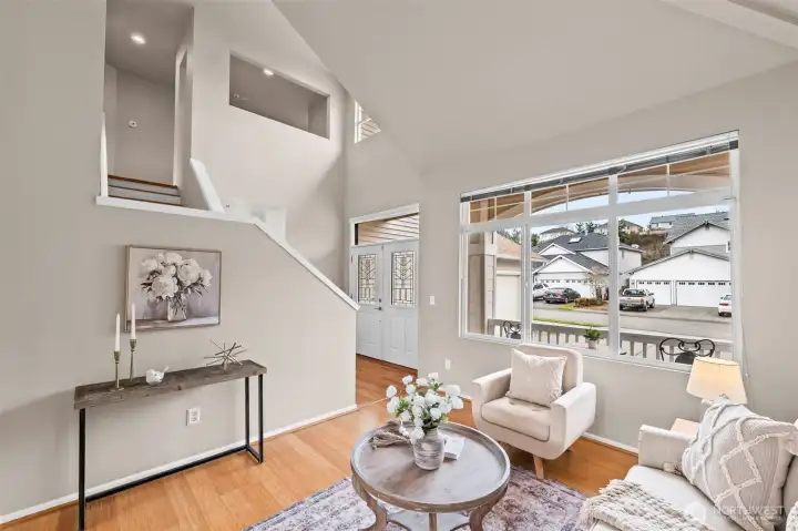 Soaring Ceilings & Natural Light. Step into a grand foyer that flows seamlessly into an elegant living area. The dramatic vaulted ceilings and oversized windows create an expansive feel, while the neutral palette and hardwood-style flooring provide a modern, sophisticated backdrop for everyday living.