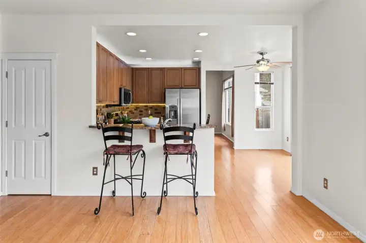 Casual Elegance. This stylish breakfast bar bridges the kitchen and living areas, offering the perfect spot for morning coffee or a quick bite. The warm wood cabinetry and granite countertops create a seamless, sophisticated look that ties the open-concept main floor together.
