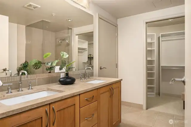 The beautiful primary bathroom featuring warm wood vanity, large mirrors and double sinks.