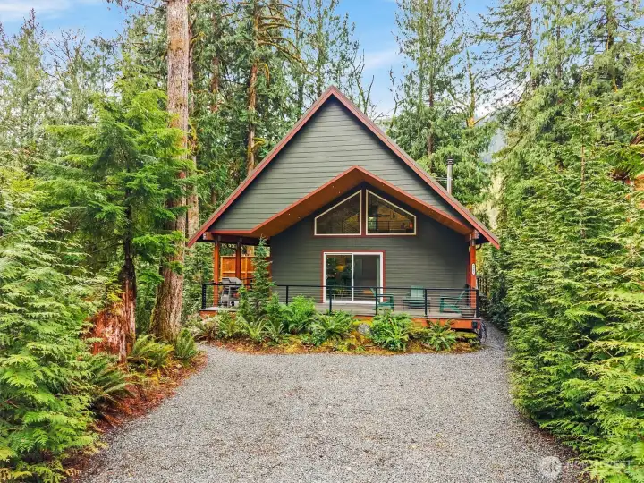 Front exterior with covered deck and forest setting.
