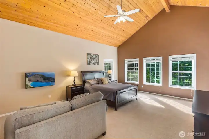 Primary suite with the soaring knotty pine clad ceilings and lots of windows. There is plenty of space here for a seating arrangement and TV