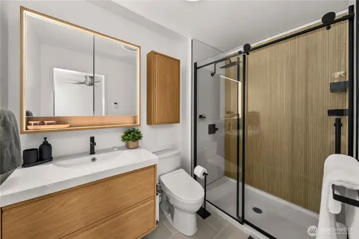 Stylish, modern bath featuring a sleek walk-in shower, warm wood accents, and a lighted mirror for a clean, contemporary feel