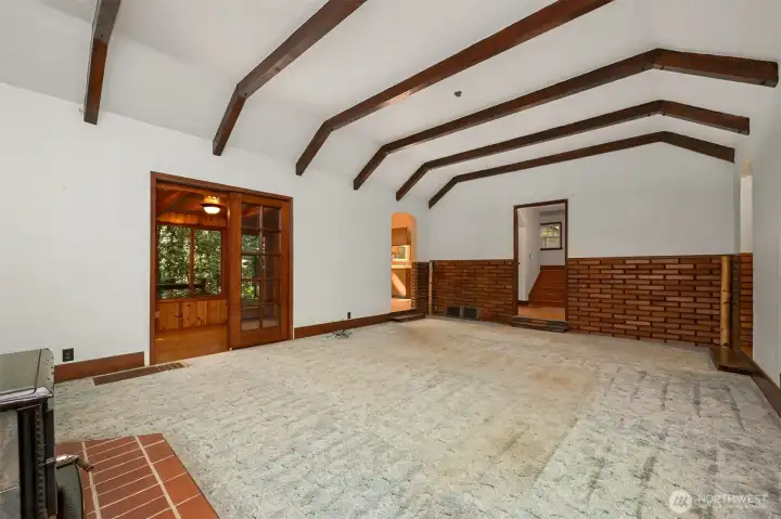 Open living room large enough for large gatherings, with timber framed ceilings, unique wooden brick, and cozy wood stove.