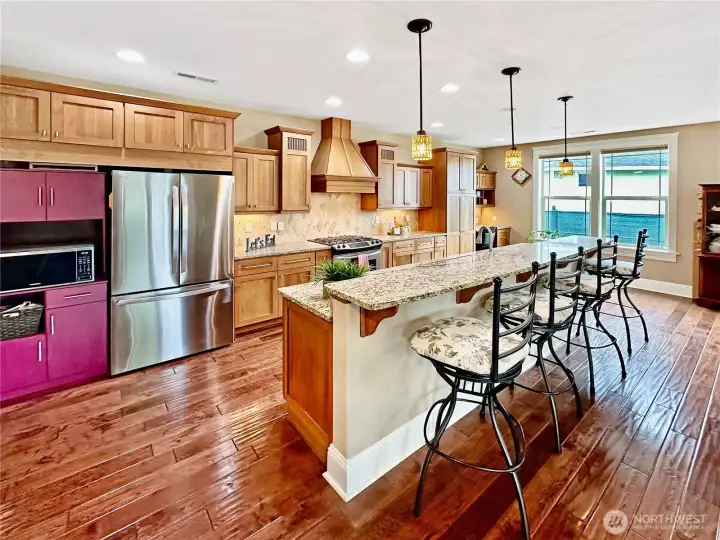 Beautiful kitchen with slab granite counters with tile back splash, island with eating bar, prep desk, stainless appliances and oak cabinets.