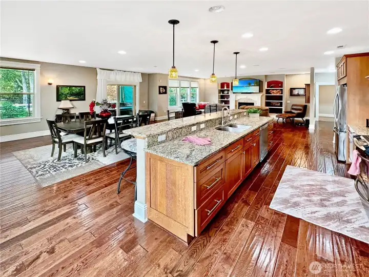View of the gathering room from the corner of the kitchen.  Notice the rich wood floors, gas fireplace with built-in surround and slider to covered rear patio.