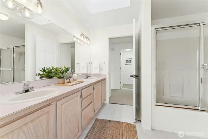 Guest bathroom with double sinks and a shower/tub combo with glass doors.