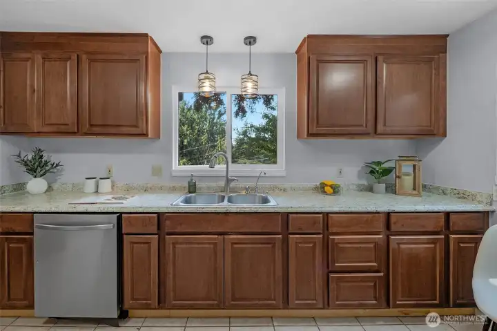 Meal prep is a breeze in this well-appointed kitchen, featuring classic wood cabinetry, expansive countertops, and a stainless steel appliances. A double sink is perfectly positioned under a bright window overlooking the yard, flanked by stylish modern pendant lights.