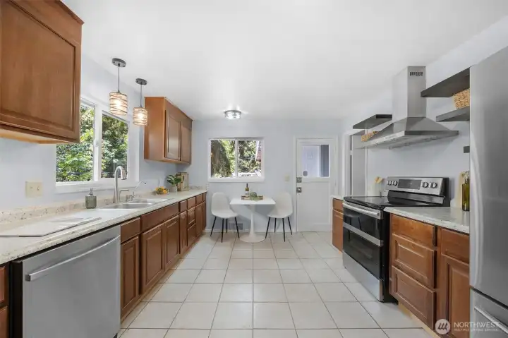 Generously sized eat-in kitchen complete with a modern range hood, floating shelves, tile floors, and a bright breakfast nook.