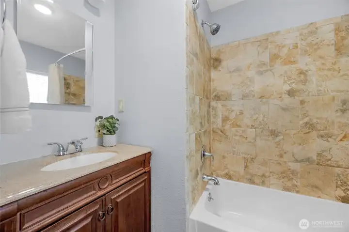 Well-maintained main floor full bathroom highlights a classic wood vanity, neutral paint, and a tub/shower combo with a beautiful tile surround. Perfectly situated for guests and daily living!