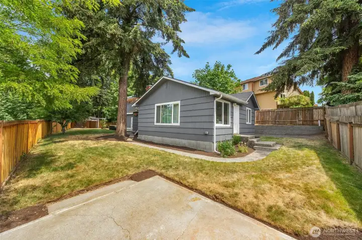 Great outdoor flexibility! The side yard boasts a separate entrance door and an open concrete patio pad that offers an ideal space for a fire pit setup. Enjoy plenty of grassy lawn space, established shade trees, and a fully fenced perimeter.