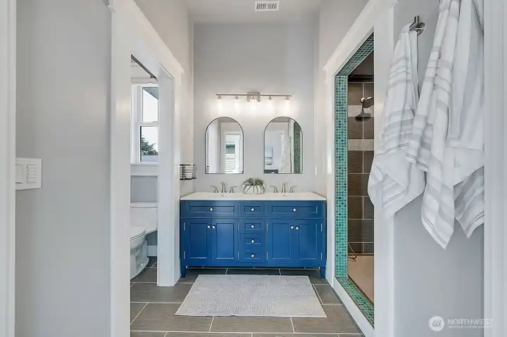 Primary bathroom with walk in tiled dual head shower, double vanity, and separate water closet.