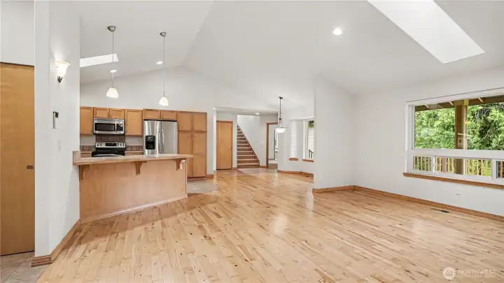 Large open living room featuring hardwood floors, soaring vaulted ceilings, and skylights that provide abundant natural light throughout.