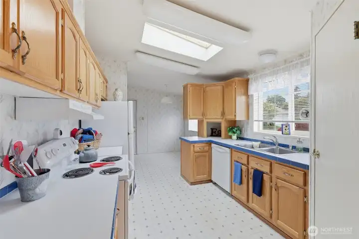 Galley style kitchen offers ample storage and prep space. Light oak cabinets include a corner bread box storage space on the open area above all cabinets. Sky lite brings in ample lighting all day! Corner walk in pantry for all you cooking needs.