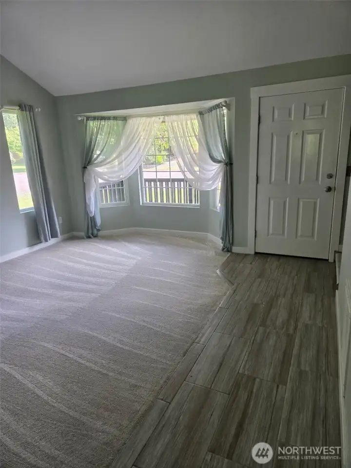 Natural light pours into this formal living room through a large bay window with charming sheer drapes. Plush carpet and luxury tile flooring create a welcoming and stylish first impression.