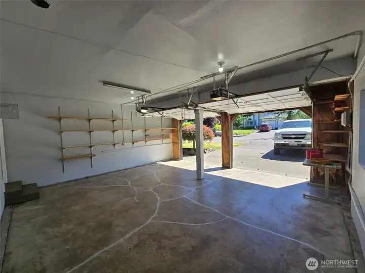 Spacious two-car garage with automatic openers and overhead lighting offers plenty of room for vehicles, tools, and hobbies. A built-in workbench and wall shelving provide ideal organization for any DIY enthusiast.