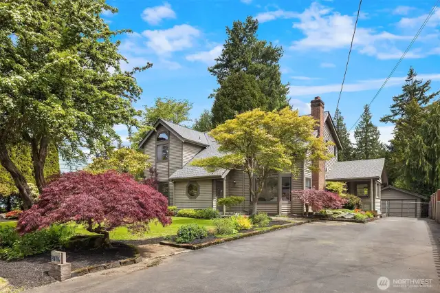 A long driveway framed by mature landscaping leads to a fully fenced yard and detached garage.