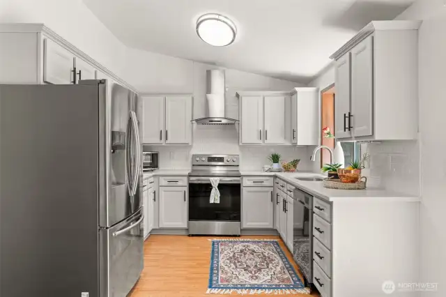Updated kitchen with stainless steel appliances, a stainless steel hood, quartz countertops, a large sink, and white tile backsplash