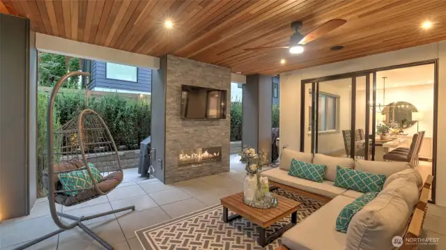 Adjacent to the kitchen and dining area, dual sliding glass doors open to a covered outdoor living room outfitted with a gas fireplace, infrared heaters, ceiling fan, and wall-mounted TV—perfect for year-round entertaining.