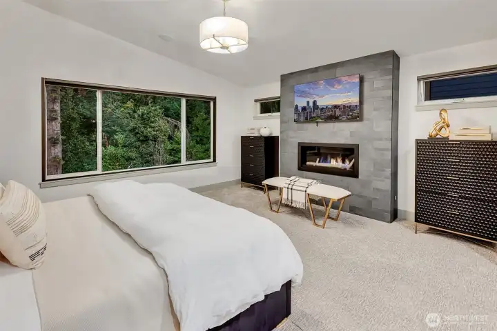 Overlooking a private forest, the serene bedroom features a floor-to-ceiling gas fireplace and remote-control black out shades.