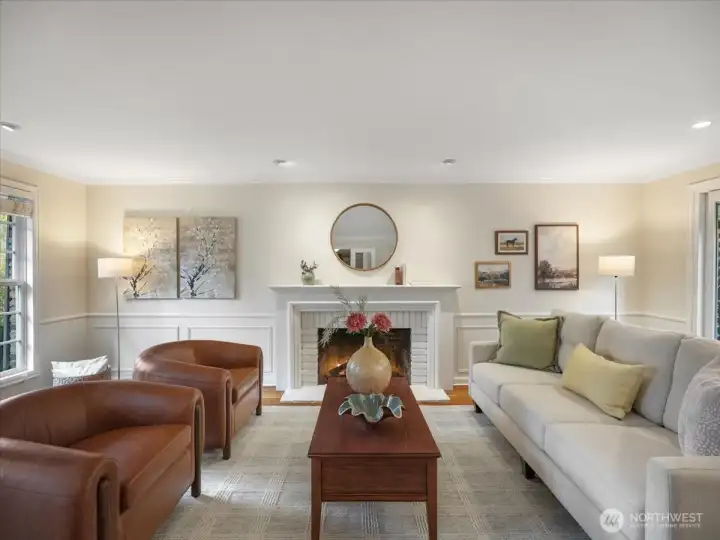 A spacious yet inviting living room—anchored by a wood-burning fireplace, with recessed lighting and classic wainscoting adding warmth and charm.