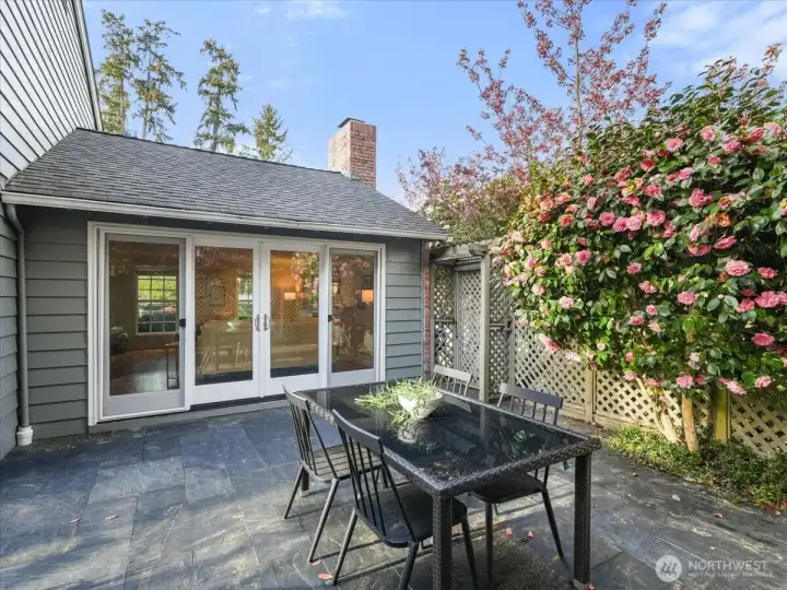 From the formal living room, French doors open to a charming outdoor dining area set beneath a stunning blooming camellia tree.