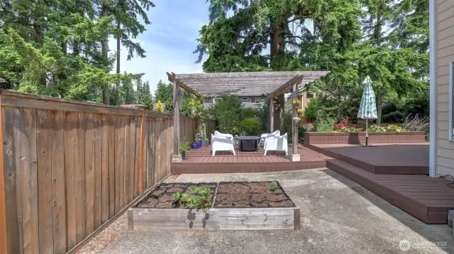 A generously sized concrete patio anchors the backyard, complemented by a beautifully crafted, standalone raised wooden planter—ideal for curated greenery or vibrant seasonal blooms