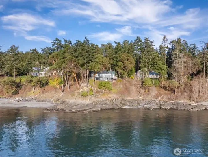 Striking west-facing residence positioned above the shoreline, surrounded by Madrona trees and layered marine vistas.