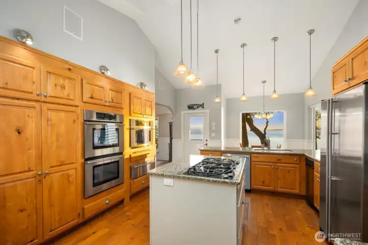 Well-appointed kitchen with custom cabinetry, double ovens, and generous prep space overlooking the open dining area and water beyond.