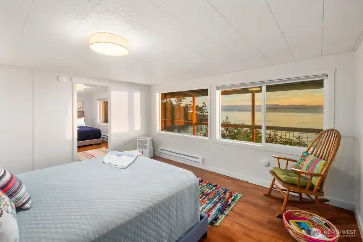 Bright bedroom featuring wide water-view windows and cozy seating area, blending indoor comfort with serene coastal scenery.