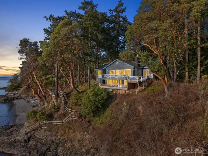 Warm interior glow meets dramatic west-facing shoreline views, showcasing the home’s inviting ambiance at sunset.