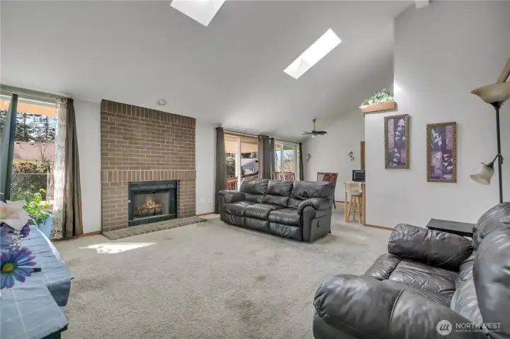Spacious living room featuring vaulted ceilings, skylights and cozy brick fireplace.