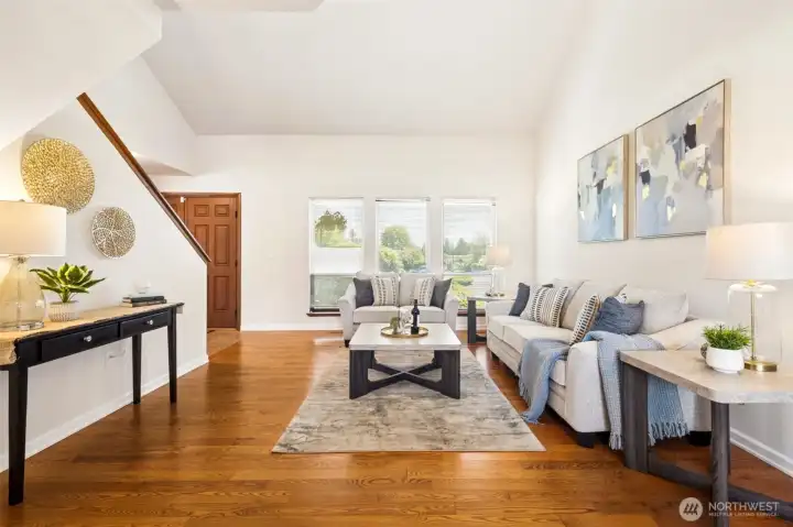 Large picture windows fill the living room with natural light while hardwood floors and vaulted ceilings add warmth and dimension.