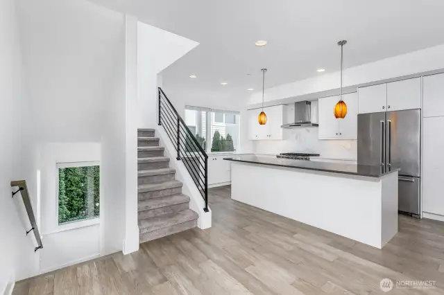 The entry stairs to the left. The stairs to the second level in the middle and the island kitchen to the right.