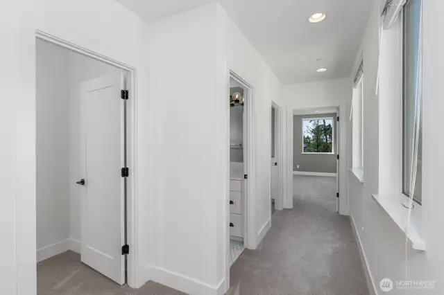 The second level hallway with the second bedroom to the left, then the full bath, the utility room and the door to the primary bedroom.