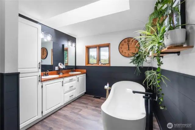 Luxurious primary spa bath featuring a skylight and dual sinks.