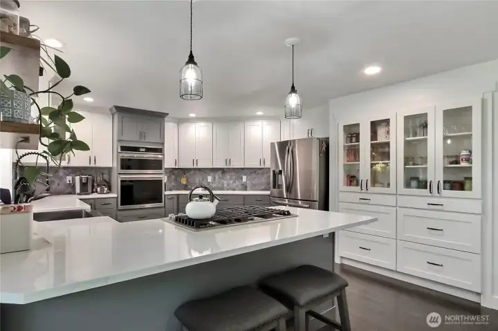 This kitchen boasts ample counter space, complemented by stylish glass cabinets that showcase beautiful dishware, and the convenience of a built-in wall oven for efficient cooking.