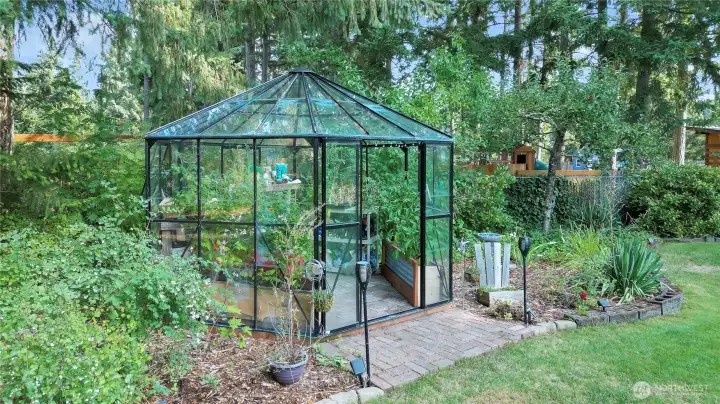 A captivating glass greenhouse, elegantly nestled amidst lush greenery, features a welcoming brick entry that adds a touch of rustic charm and architectural interest to the scene.