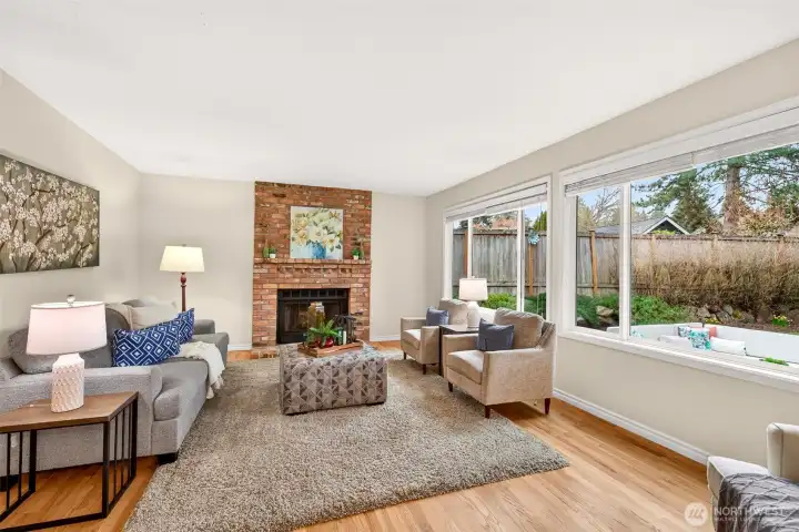 The adjacent family room is warm and comfortable, anchored by a classic brick fireplace and large backyard facing windows that bring in soft natural light. It is a true everyday living space, well suited for relaxing, gathering, and spending time together.
