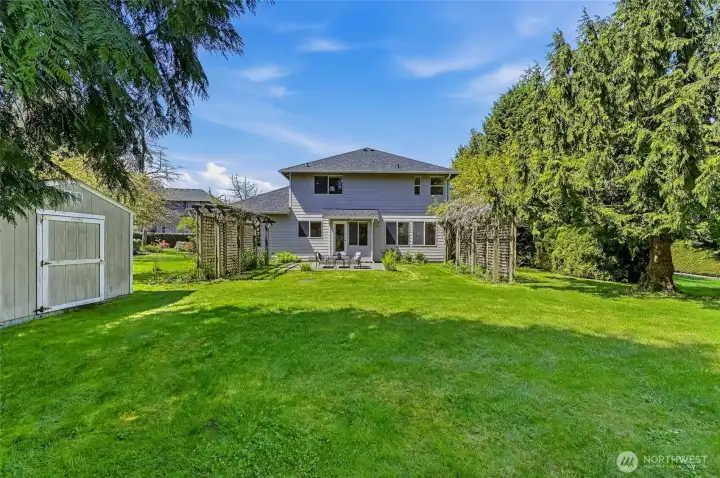 Rear home view from the vegetable garden, showcasing a yard that is notably more expansive on the sides than appears in frame. Wisteria gracefully drapes over the trellis. Storage shed will convey to Buyer.