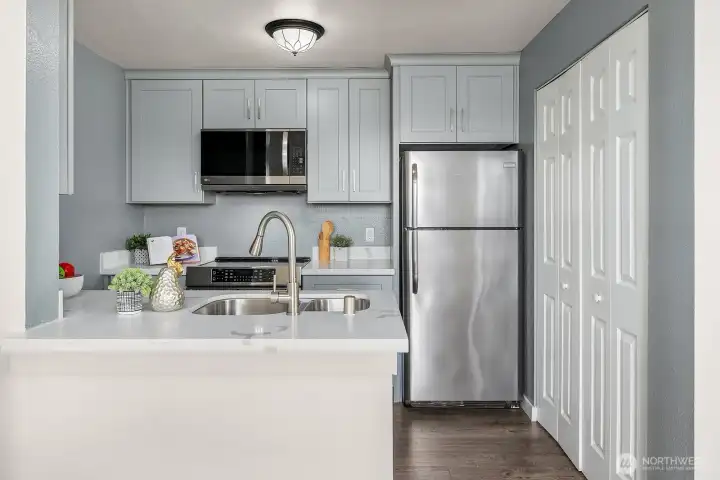 Kitchen showcasing a convenient breakfast bar, stainless steel appliances, and soft gray cabinetry creating a clean and modern aesthetic. Kitchen showcasing a convenient breakfast bar, stainless steel appliances, and soft gray cabinetry creating a clean and modern aesthetic.