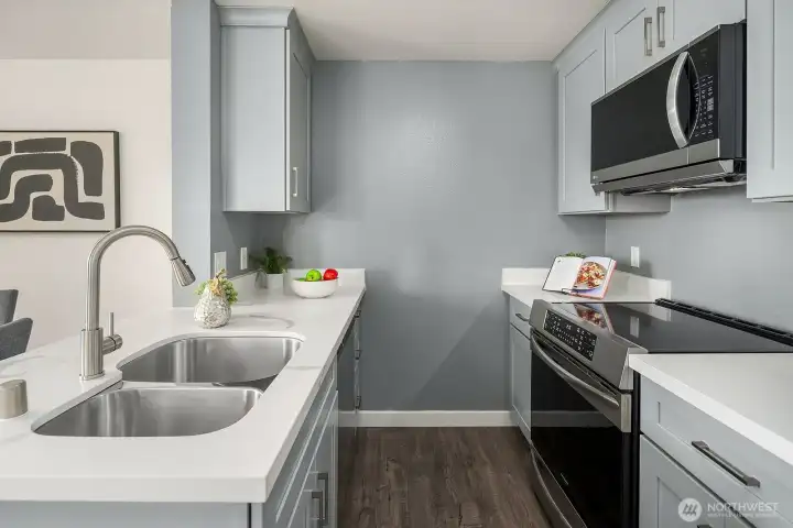 Close-up of the kitchen highlighting the quartz countertops, undermount sink, and stainless steel appliances set against elegant gray cabinetry. Close-up of the kitchen highlighting the quartz countertops, undermount sink, and stainless steel appliances set against elegant gray cabinetry.