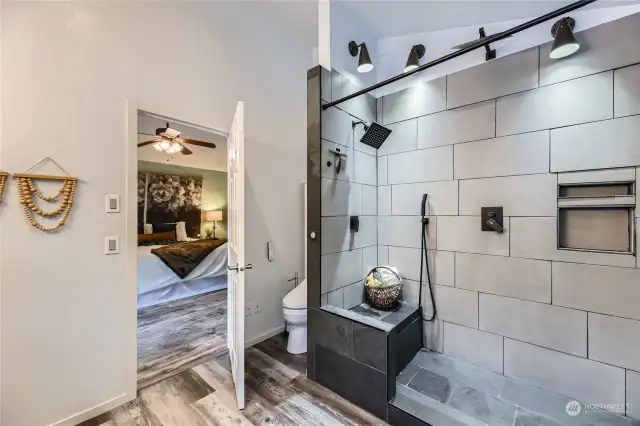 This freshly updated primary bath includes a walk-in shower with designer tile, a built-in bench, and double niches, blending convenience with contemporary design.